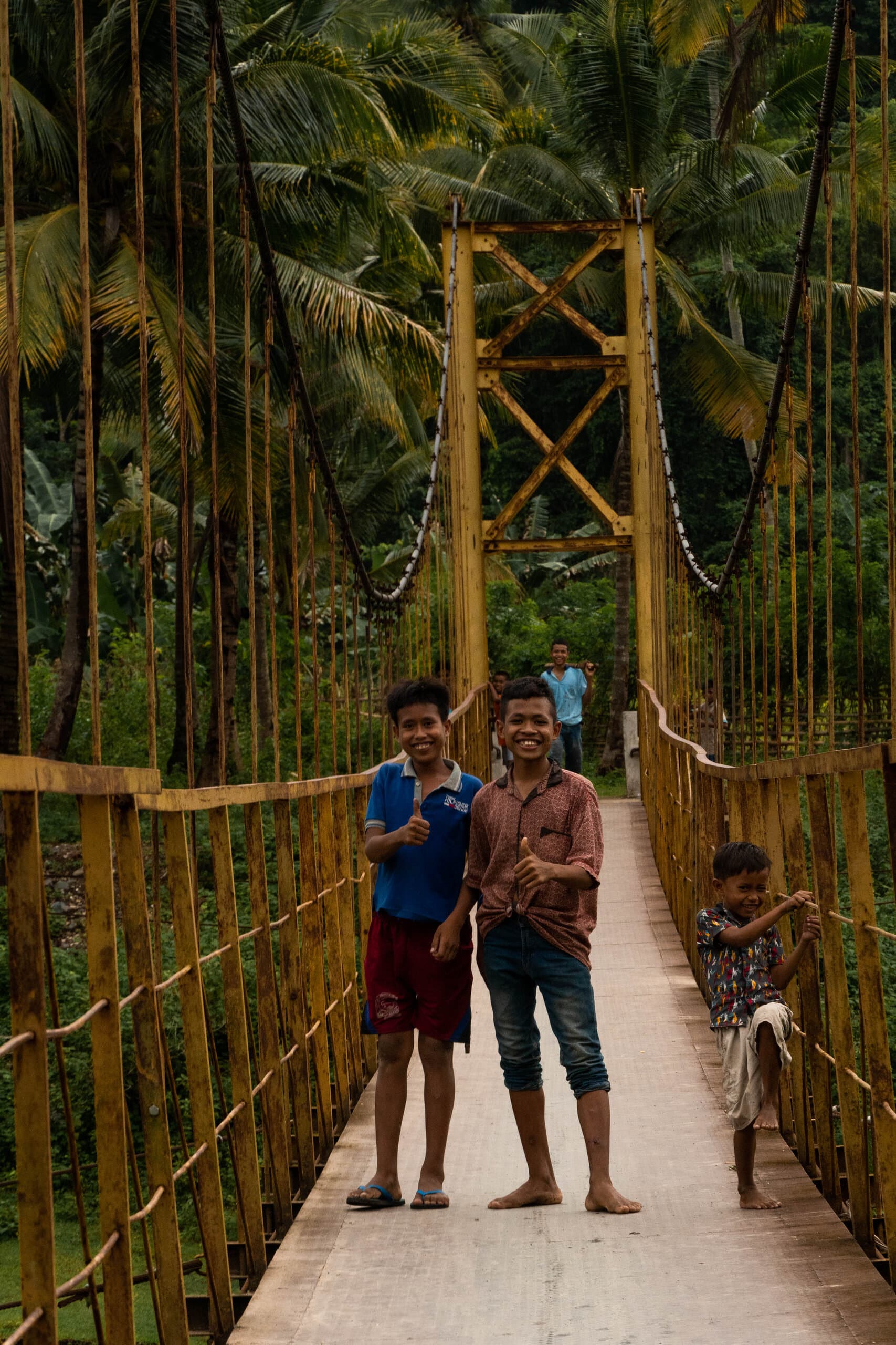 Local kids on traditional wooden bridge surrounded by palm trees in Sumba