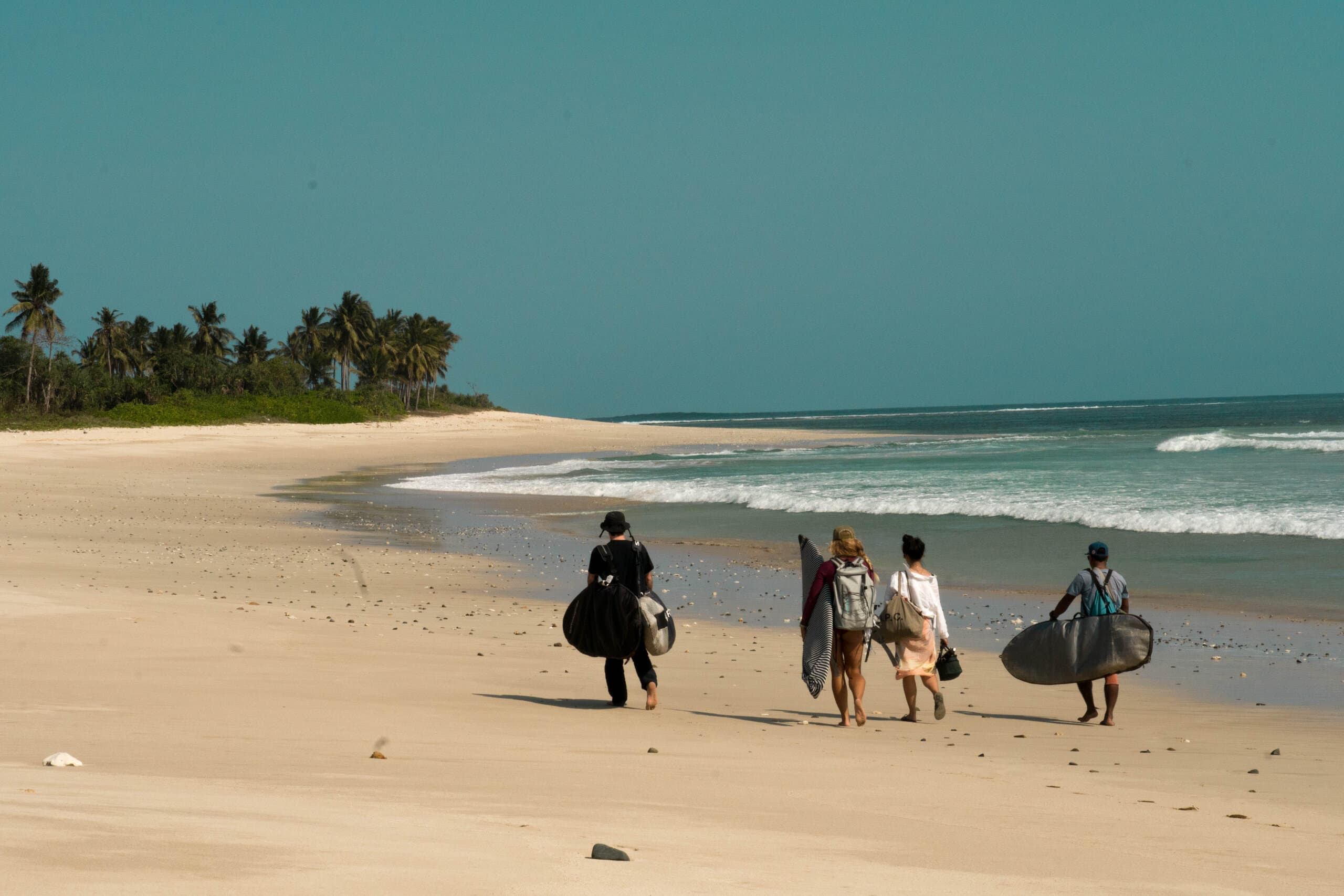 Surfer walking along Cocos Beach in Sumba, Indonesia